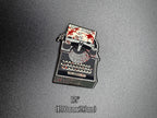 Enamel pin of a typewriter with text on a gray background