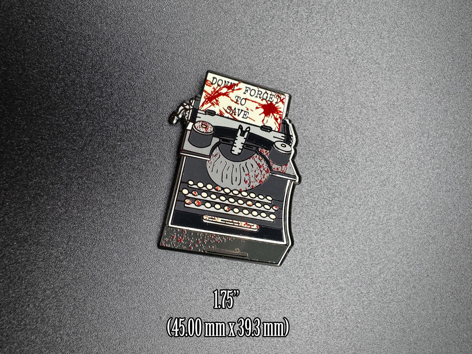 Enamel pin of a typewriter with text on a gray background