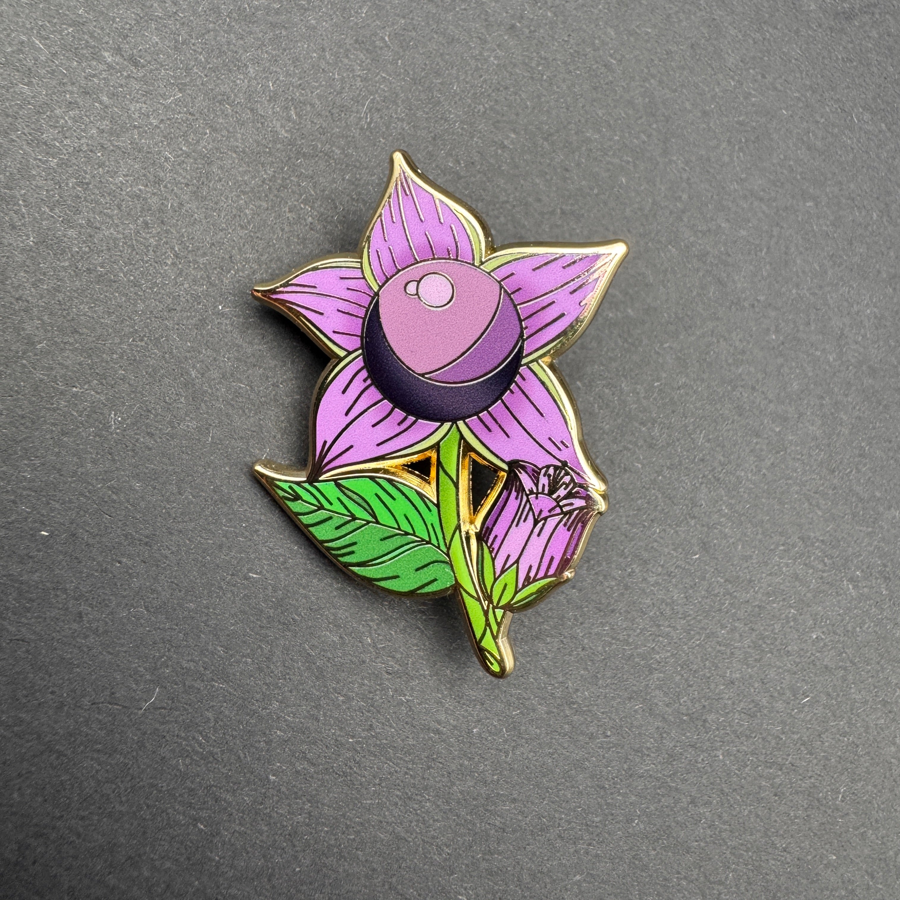 Floral-themed pin with purple flower and green leaves on a gray background